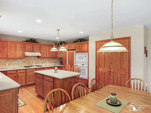 9241 Legacy Ct, Temperance, MI 48182 - kitchen with built in appliances, under cabinet range hood, light countertops, brown cabinetry, and a kitchen island