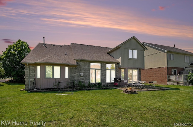 47040 W Wayford Dr, Shelby Twp, MI 48315 - back of property at dusk featuring brick siding, an outdoor fire pit, a lawn, and a patio area