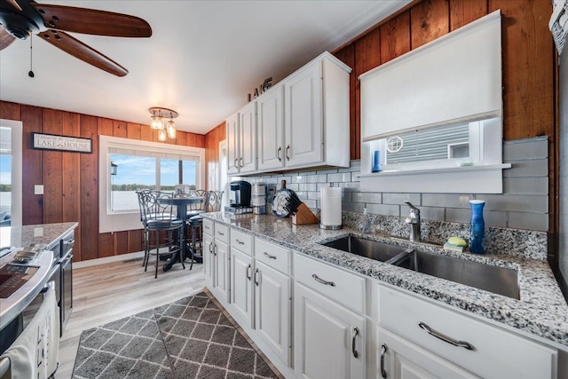 4805 Pinellas Dr, Hale, MI 48739 - kitchen featuring decorative backsplash, a sink, white cabinets, light wood finished floors, and wood walls