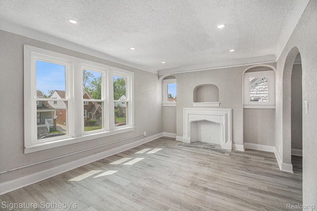 16762 Woodingham Dr, Detroit, MI 48221 - unfurnished living room featuring a textured ceiling, healthy amount of natural light, baseboards, wood finished floors, and arched walkways