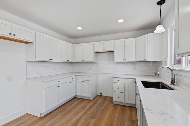2023 Green Acres Dr, Adrian, MI 49221 - kitchen featuring a sink, light stone countertops, light wood-style floors, decorative backsplash, and white cabinetry