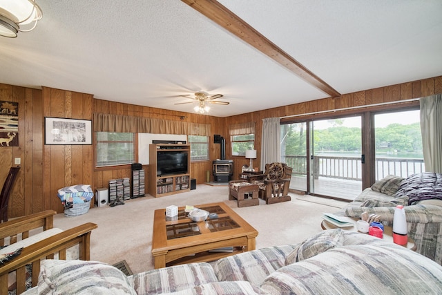 6387 N Larson Rd, Fountain, MI 49410 - carpeted living room with a wood stove, wooden walls, ceiling fan, and beamed ceiling