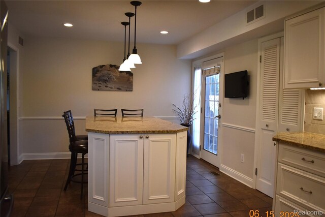 6560 Perham Dr, West Bloomfield, MI 48322 - kitchen with dark tile patterned floors, white cabinetry, light stone counters, a kitchen island, and decorative light fixtures