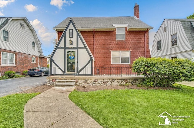 448 Borgess Ave, Monroe, MI 48162 - tudor house with a chimney, brick siding, a front yard, a shingled roof, and covered porch