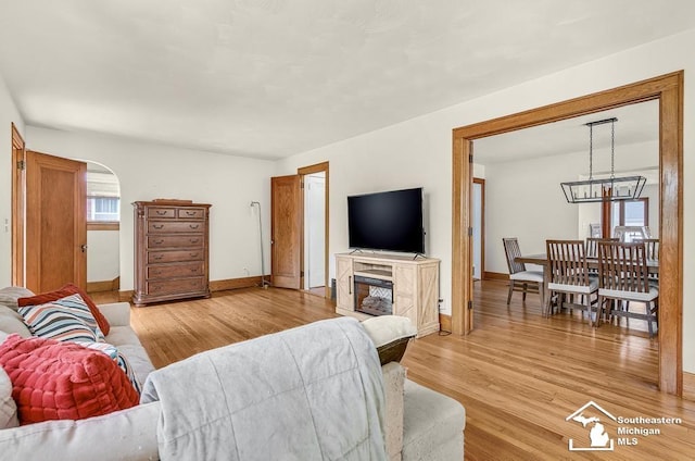 448 Borgess Ave, Monroe, MI 48162 - living room featuring baseboards, light wood-type flooring, arched walkways, a chandelier, and a glass covered fireplace