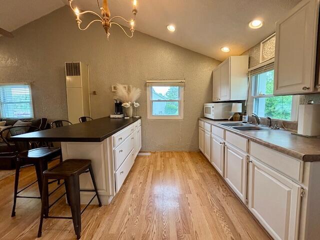 824 N Werners Landing Dr, Bronson, MI 49028 - kitchen with vaulted ceiling, light wood finished floors, a peninsula, white microwave, and a breakfast bar area