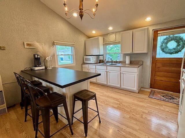 824 N Werners Landing Dr, Bronson, MI 49028 - kitchen with white microwave, lofted ceiling, white cabinetry, a chandelier, and light wood-style flooring