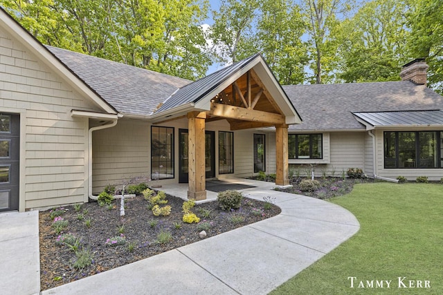 582 Campbell Rd, Saugatuck, MI 49453 - view of exterior entry featuring roof with shingles, a lawn, and a chimney
