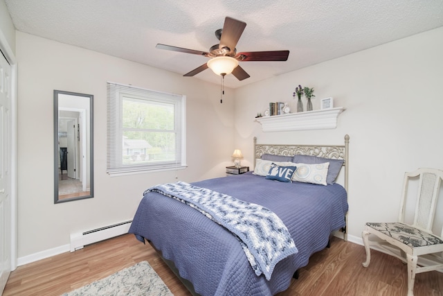 819 Elm St, Manistee, MI 49660 - bedroom with a baseboard radiator, wood finished floors, a textured ceiling, a ceiling fan, and baseboards