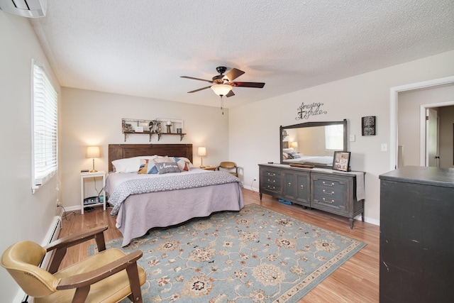 819 Elm St, Manistee, MI 49660 - bedroom featuring light wood-style flooring, a textured ceiling, a wall mounted air conditioner, ceiling fan, and baseboard heating