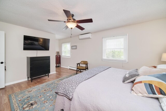 819 Elm St, Manistee, MI 49660 - bedroom featuring a wall unit AC, baseboard heating, wood finished floors, baseboards, and a textured ceiling