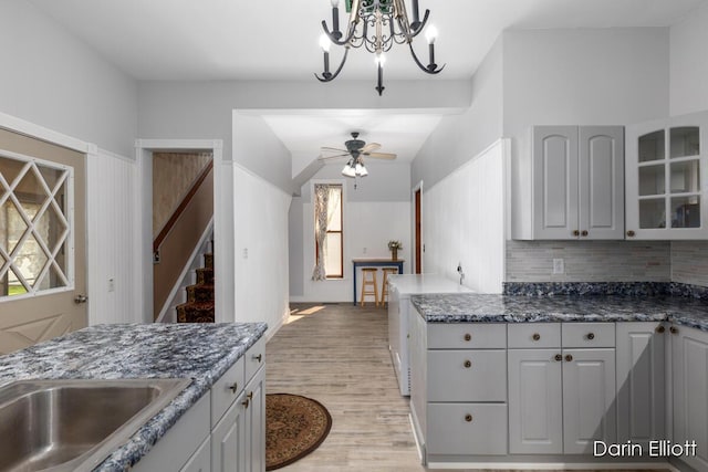 216 E Main St, Ionia, MI 48846 - kitchen featuring light wood-style flooring, a chandelier, glass insert cabinets, a ceiling fan, and tasteful backsplash