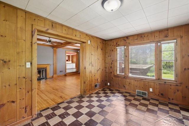 2505 Court St, Saginaw, MI 48602 - unfurnished room featuring tile patterned floors, wood walls, a glass covered fireplace, baseboards, and ceiling fan