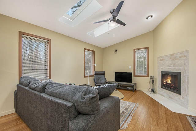 7362 30th St SE, Ada, MI 49301 - living room featuring vaulted ceiling, a tile fireplace, light wood-style floors, a skylight, and a ceiling fan