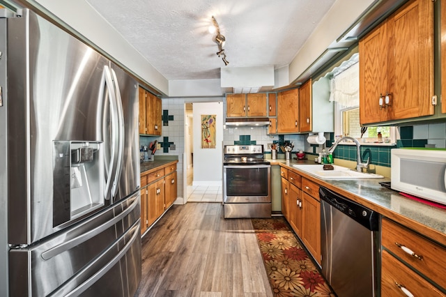 50902 Magician Lk Rd, Dowagiac, MI 49047 - kitchen featuring stainless steel appliances, a sink, under cabinet range hood, brown cabinetry, and backsplash