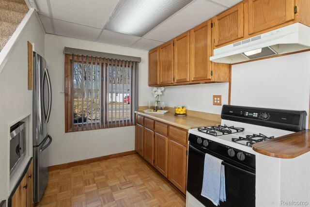2830 N Duck Lake Rd, Highland, MI 48356 - kitchen featuring stainless steel appliances, under cabinet range hood, light countertops, brown cabinetry, and a paneled ceiling