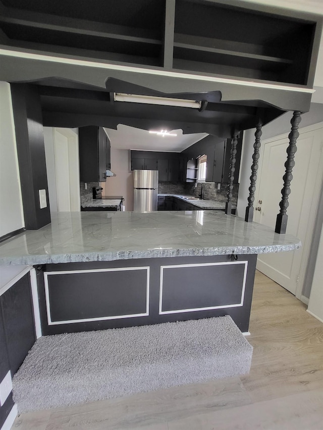 1010 S Pearce St, Owosso, MI 48867 - kitchen with freestanding refrigerator, dark cabinetry, a peninsula, and light stone counters