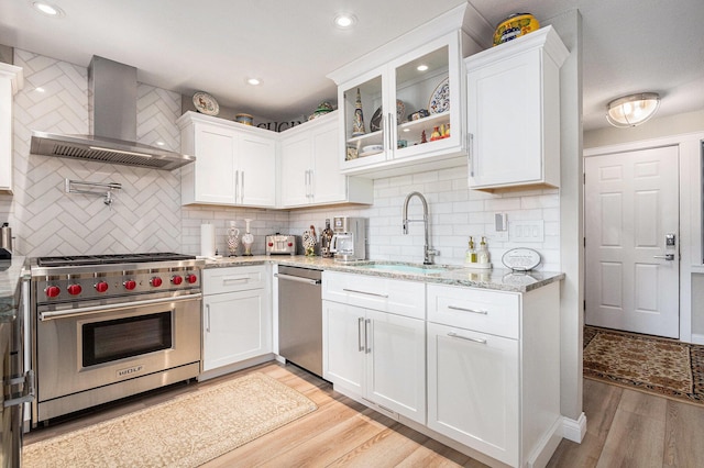 144 Dunkley Ave Unit 4, South Haven, MI 49090 - kitchen with appliances with stainless steel finishes, wall chimney range hood, white cabinetry, light wood-style floors, and tasteful backsplash