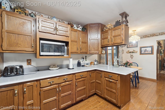 14210 W Burt Rd W, Chesaning, MI 48616 - kitchen with stainless steel microwave, a peninsula, light countertops, brown cabinets, and light wood-style floors