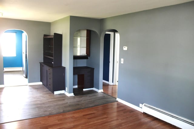 6994 E 34th Rd, Cadillac, MI 49601 - unfurnished living room with baseboard heating, a baseboard radiator, arched walkways, wood finished floors, and baseboards