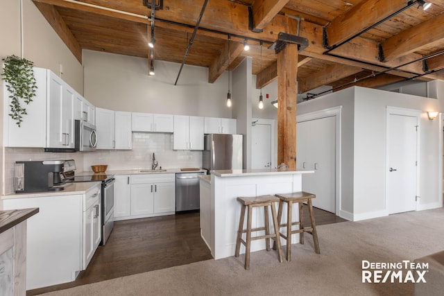 940 Monroe Ave NW Unit 335, Grand Rapids, MI 49503 - kitchen featuring appliances with stainless steel finishes, track lighting, dark colored carpet, a kitchen breakfast bar, and a wooden ceiling with exposed beams