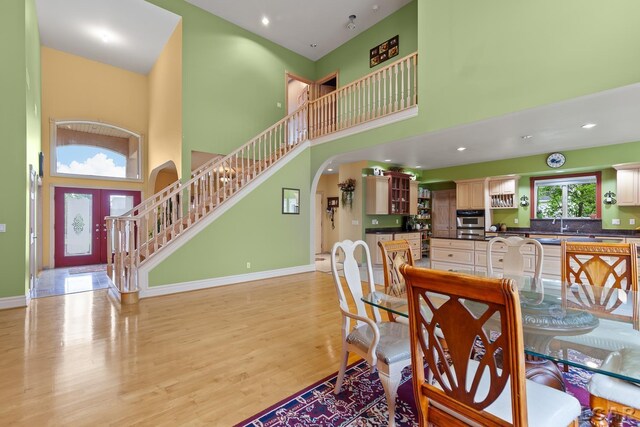 1269 Scott Ridge Dr, Adrian, MI 49221 - dining area with arched walkways, a towering ceiling, stairs, light wood-type flooring, and baseboards