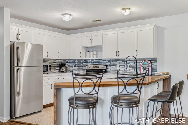 5869 Crosswinds Dr Unit 21, Norton Shores, MI 49444 - kitchen with appliances with stainless steel finishes, butcher block countertops, white cabinets, a breakfast bar, and open shelves