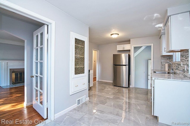 8035 Pinehurst St, Detroit, MI 48204 - kitchen with freestanding refrigerator, white cabinetry, decorative backsplash, light stone counters, and a glass covered fireplace