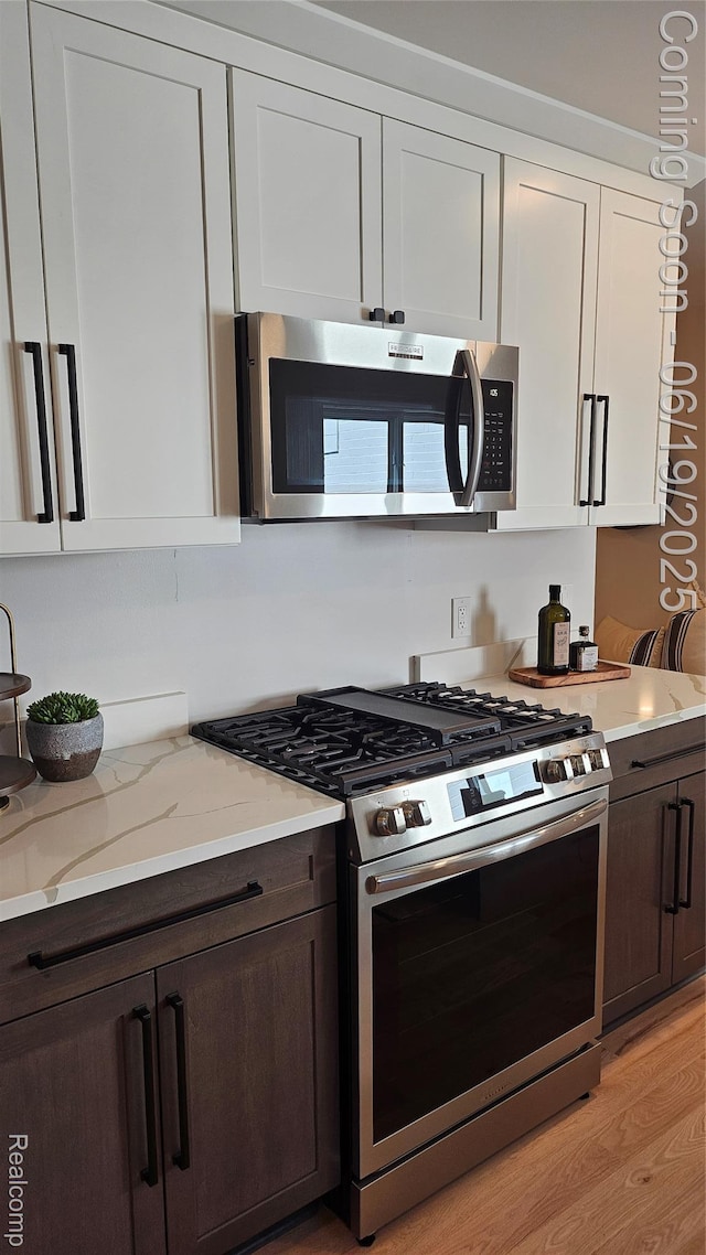54232 Mound Rd, Shelby Twp, MI 48316 - kitchen with stainless steel appliances, dark brown cabinets, white cabinetry, light stone counters, and light wood finished floors
