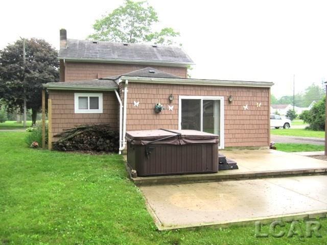 311 Tiffin St, Hudson, MI 49247 - back of house featuring a hot tub, a patio area, a lawn, a chimney, and roof with shingles
