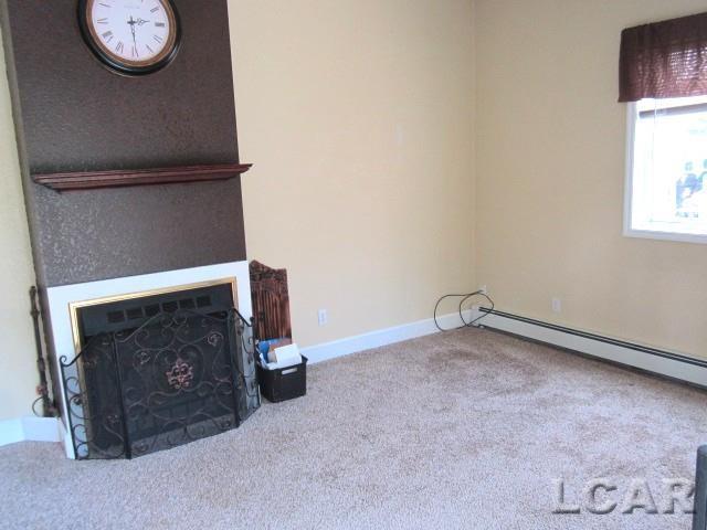 311 Tiffin St, Hudson, MI 49247 - unfurnished living room featuring carpet, a fireplace, a baseboard heating unit, and baseboards