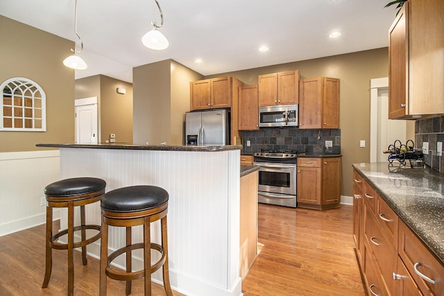 23 Kenneth St, Pentwater, MI 49449 - kitchen featuring appliances with stainless steel finishes, a kitchen bar, light wood-style flooring, tasteful backsplash, and brown cabinetry