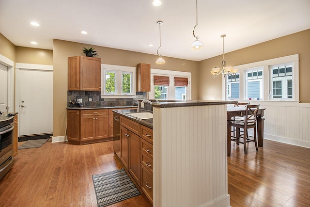 23 Kenneth St, Pentwater, MI 49449 - kitchen featuring wood finished floors, dark countertops, brown cabinets, an island with sink, and a chandelier