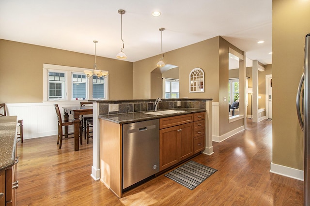 23 Kenneth St, Pentwater, MI 49449 - kitchen with stainless steel dishwasher, a sink, a wainscoted wall, brown cabinetry, and a chandelier