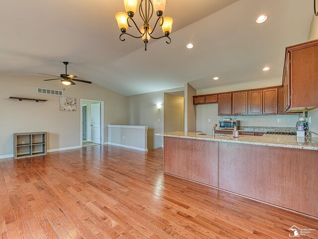 8721 E Park Ridge Cir, Newport, MI 48166 - kitchen with brown cabinetry, stainless steel microwave, light stone counters, vaulted ceiling, and open floor plan