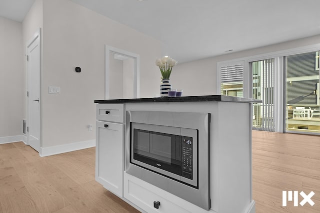 627 Fairview Ave NE Unit 2, Grand Rapids, MI 49503 - detailed view of light wood-style flooring, baseboards, white cabinetry, and stainless steel microwave