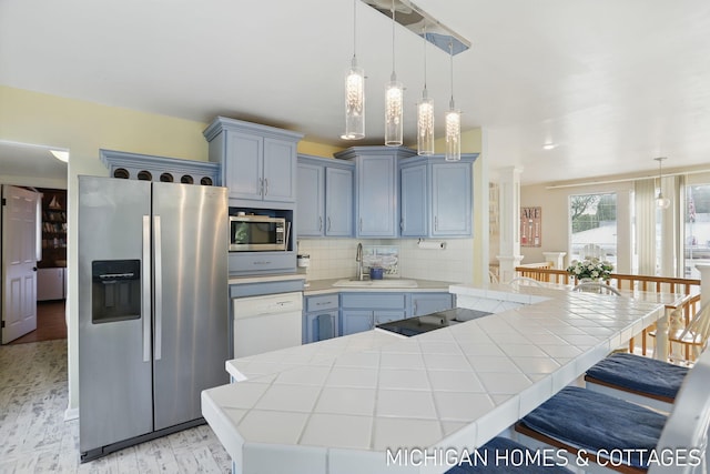 2259 Ottawa Beach Rd, Holland, MI 49424 - kitchen with appliances with stainless steel finishes, decorative columns, a kitchen breakfast bar, a sink, and tile countertops