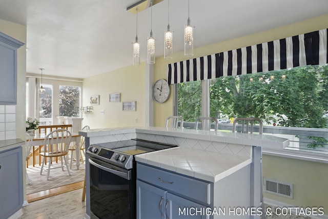 2259 Ottawa Beach Rd, Holland, MI 49424 - kitchen with electric stove, light wood-style flooring, blue cabinetry, tile counters, and hanging light fixtures