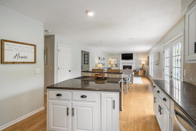 5616 Stoney Brook Rd, Kalamazoo, MI 49009 - kitchen with stainless steel dishwasher, light wood-type flooring, a kitchen island, a glass covered fireplace, and white cabinets