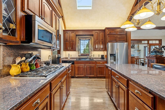 6242 131st Ave, Saugatuck, MI 49453 - kitchen with appliances with stainless steel finishes, a sink, light wood-style flooring, pendant lighting, and dark stone counters
