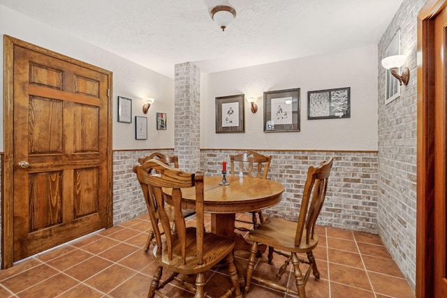 6242 131st Ave, Saugatuck, MI 49453 - tiled dining space featuring a textured ceiling, a wainscoted wall, and brick wall