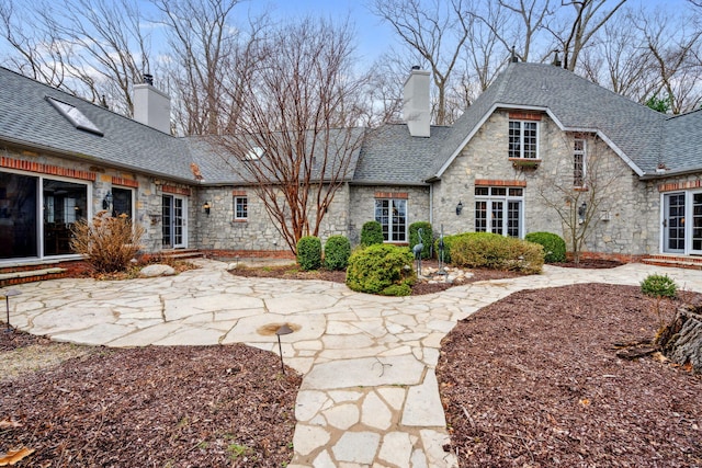 6242 131st Ave, Saugatuck, MI 49453 - back of house with stone siding, a chimney, and roof with shingles