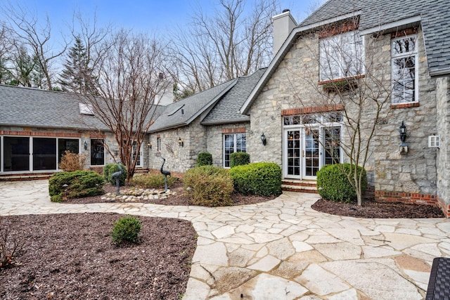 6242 131st Ave, Saugatuck, MI 49453 - back of house with stone siding, a chimney, and roof with shingles