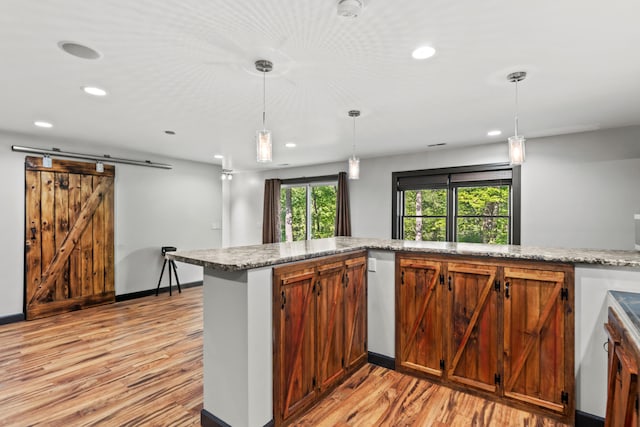 2980 N Old State Rd, Weidman, MI 48893 - kitchen featuring a barn door, light wood-style flooring, recessed lighting, decorative light fixtures, and light stone countertops