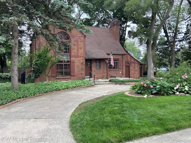 27943 Sunset Blvd W, Lathrup Village, MI 48076 - tudor home with brick siding, a chimney, concrete driveway, a front lawn, and roof with shingles