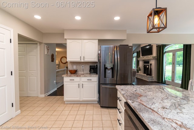75757 Peters Dr, Bruce, MI 48065 - kitchen featuring stainless steel fridge, light tile patterned flooring, white cabinets, light stone counters, and a fireplace with raised hearth