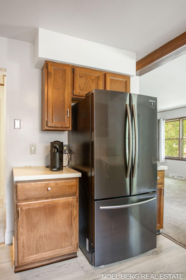 1710 Dykhouse Ave, Grand Haven, MI 49417 - kitchen featuring freestanding refrigerator, light countertops, brown cabinetry, light wood finished floors, and beam ceiling