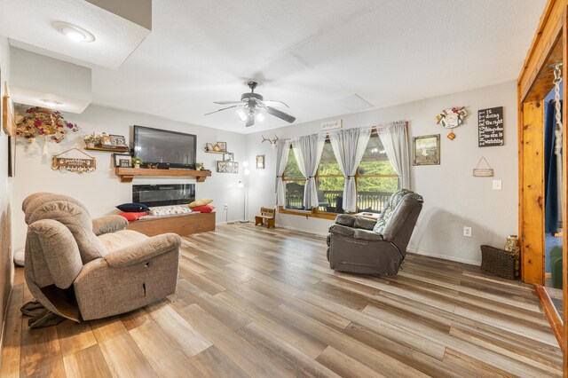 22251 210th Ave, Tustin, MI 49688 - living room featuring a ceiling fan, light wood-type flooring, a glass covered fireplace, and baseboards