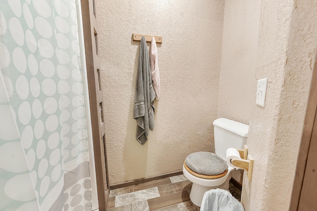 22251 210th Ave, Tustin, MI 49688 - bathroom featuring toilet, a textured wall, a shower with shower curtain, and baseboards