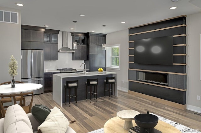 3634 Trumbull St Unit 65, Detroit, MI 48208 - kitchen with appliances with stainless steel finishes, wall chimney range hood, a sink, a breakfast bar area, and light wood-type flooring
